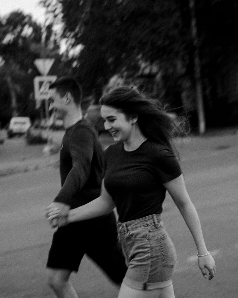 Happy young couple running and holding hands in a black and white street scene.