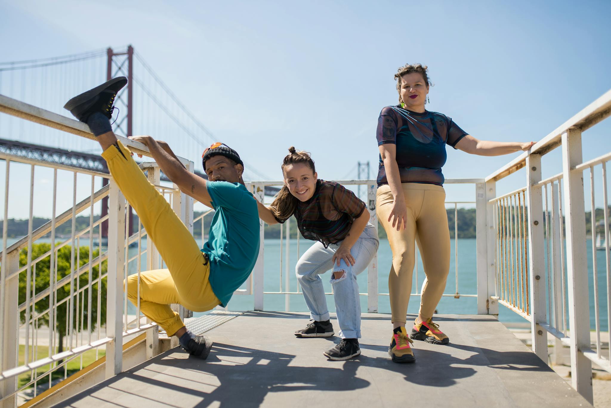 Three friends express joy and style in a dynamic pose on the Lisbon Bridge.